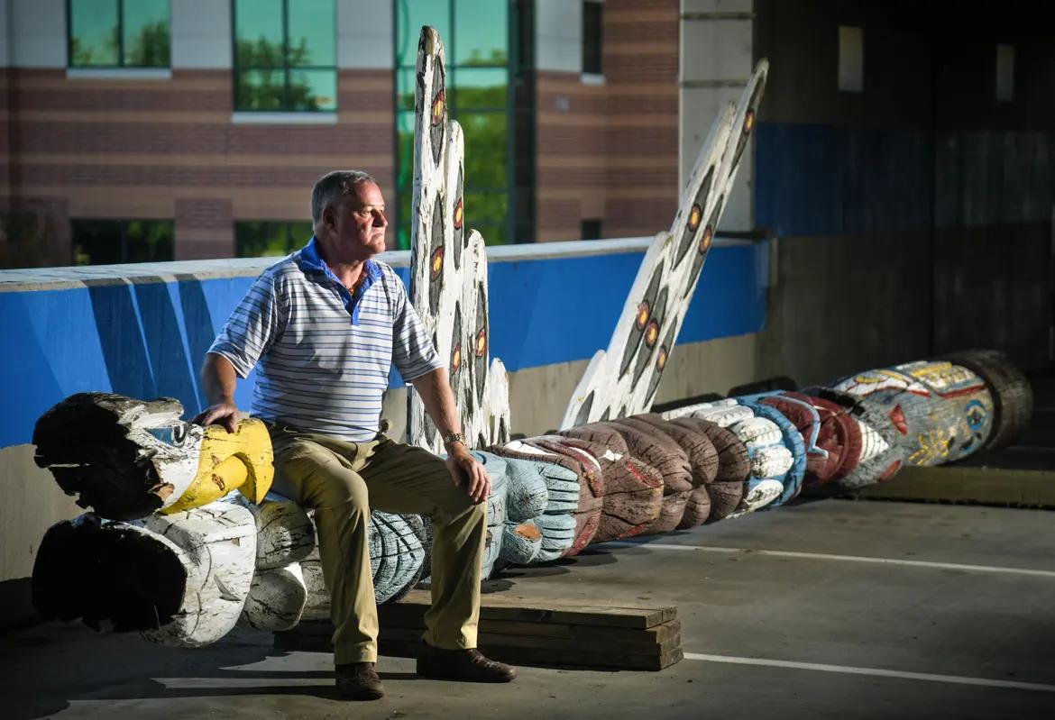 This 2019 photograph from the Spokesman-Review depicts the totem pole after its removal. The man seated on it is Kent Hull, one of the original organizers of its donation.